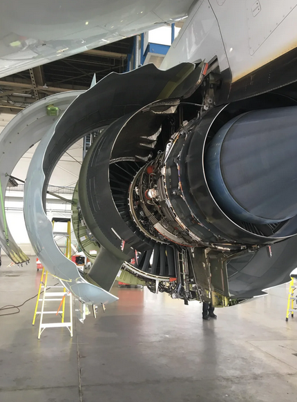 Open aircraft engine thrust reverser assembly in maintenance hangar with cowl open