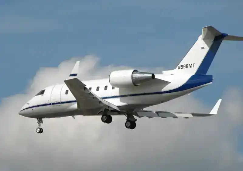 Bombardier / Canadair CL-600 Challenger business jet (registration N598MT) on approach to land — white airframe with dark blue cheatline and tail trim, side profile against cumulus cloud sky