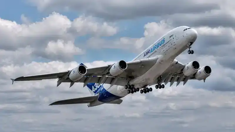 Airbus A380 in Airbus house livery climbing away with landing gear retracting — dramatic underside view showing all four Trent/GP7200 engines and the double-deck fuselage