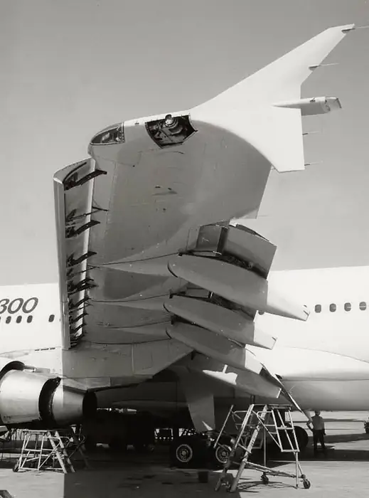 Airbus A380 rear fuselage and empennage during assembly — vertical stabiliser fitted, horizontal stabilisers attached, and trailing-edge high-lift devices deployed for inspection; photographed at Airbus assembly facility with maintenance scaffolding around the airframe