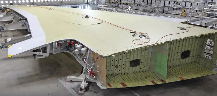 A380 wing primary structure during build — upper cover skin panel and front spar visible on assembly jig at Airbus Broughton, with integrated stringer-stiffened section shown in cutaway view
