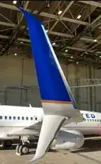 Close-up of United Airlines Boeing 737 split-scimitar winglet on the apron — blue and white livery showing the upper blade and lower ventral strake of the APB design