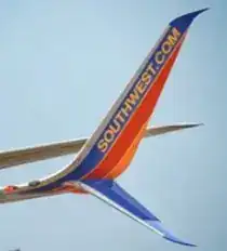 Southwest Airlines Boeing 737 split-scimitar winglet in flight — SOUTHWEST.COM branding on the upper winglet blade, against clear blue sky