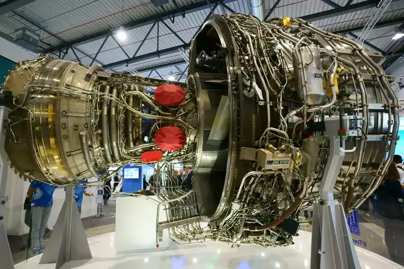 Rolls-Royce Trent XWB three-shaft turbofan on display stand — bare engine showing core hot-section, accessory gearbox, fuel and oil pipework, and combustion chamber arrangement (representative of the Trent family architecture)