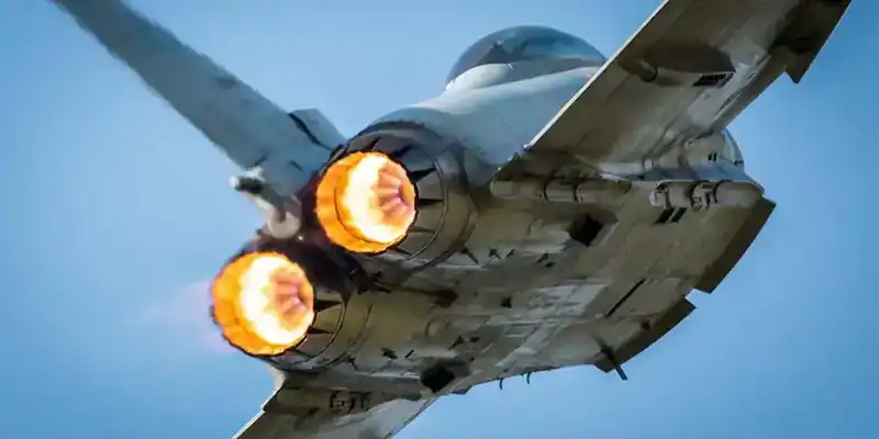 Eurofighter Typhoon in flight from below, both Eurojet EJ200 turbofan engines in full afterburner showing bright orange exhaust flames — twin nozzles, ventral intake, side profile of the rear fuselage