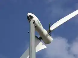 Close-up of a wind turbine nacelle and hub assembly mounted on tower top — white nacelle housing with one blade extending out of frame, gearbox and yaw mechanism visible