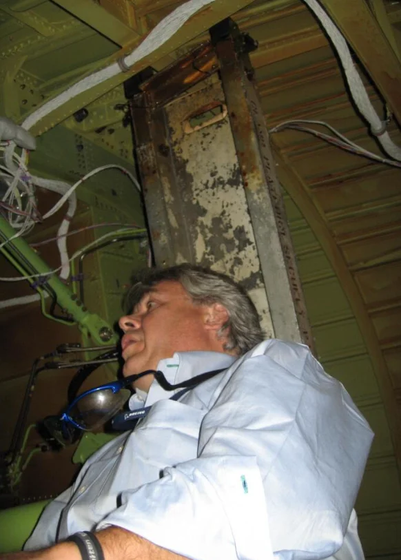 Steve Clamp inside the aft fuselage beneath the Station 2598 bulkhead structure, surrounded by wiring looms and frame members during an internal inspection