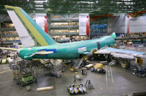 Boeing 747 fuselage in green protective primer on the Everett production line, surrounded by work platforms and factory tooling